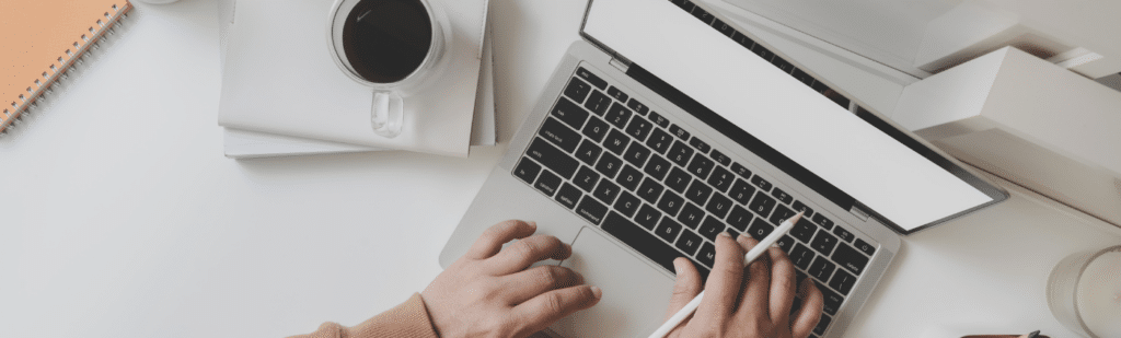 Person typing on a laptop next to a cup of coffee