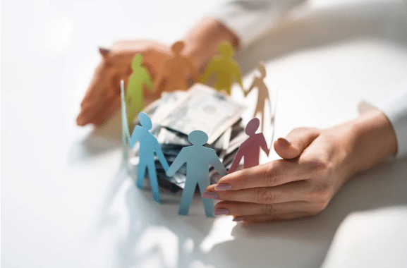 two hands surround a circle of rainbow paper people standing around a pile of money